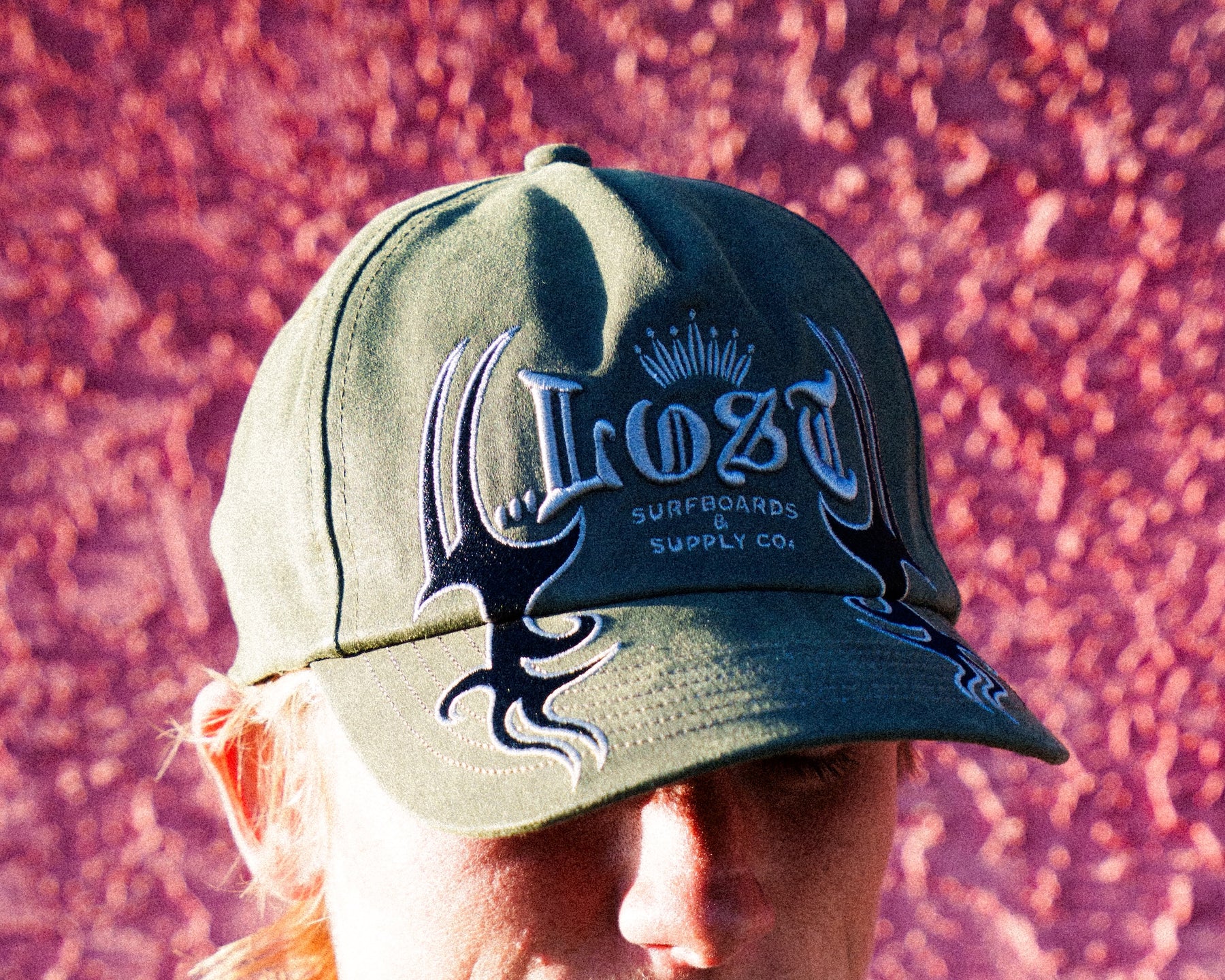Person wearing green hat against pink wall