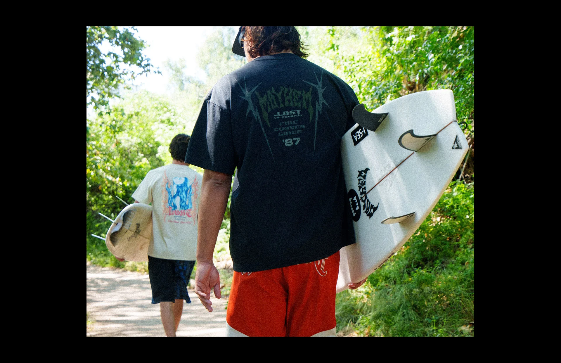 Two people carrying surfboards on path